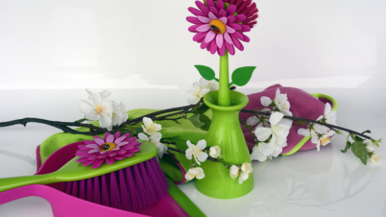 Spring cleaning challenge supplies like rags, broom, dustpan and a pretty flowered scrubbing brush in a vase.