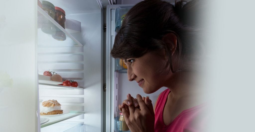 Woman standing with the fridge open at night.