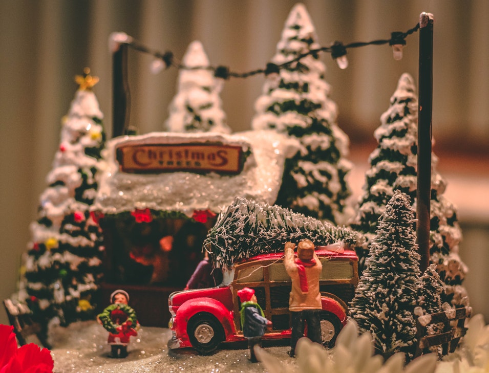 Miniature Christmas display with a Christmas tree lot and a family loading up a tree on top of their car. 