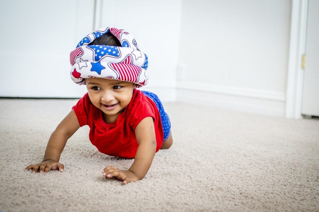 Baby crawling on the floor with a hat on its head. He looks like he is going after some toys for kids his age.