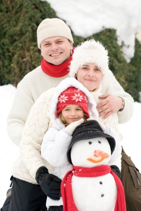 Family dressed in white sweaters dad mom and daughter with a snowman posing for a holiday family picture outside in the snow