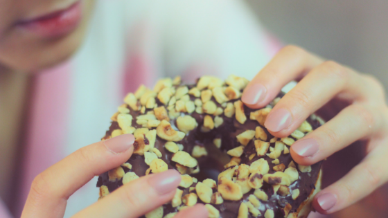 Woman eating a chocolate donut with nuts. Is this one of the signs of emotional eating? Read on to see.